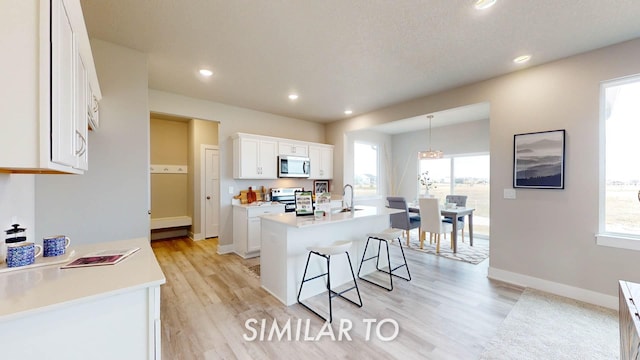 kitchen with pendant lighting, white cabinetry, plenty of natural light, stainless steel appliances, and an island with sink