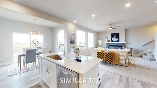 kitchen featuring decorative light fixtures, white cabinetry, dishwasher, sink, and a kitchen island with sink