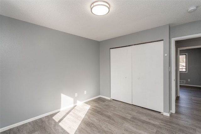 unfurnished bedroom featuring light wood-type flooring, a textured ceiling, and a closet