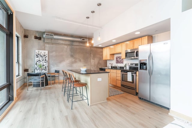 kitchen featuring appliances with stainless steel finishes, a center island, light hardwood / wood-style floors, light brown cabinetry, and decorative light fixtures