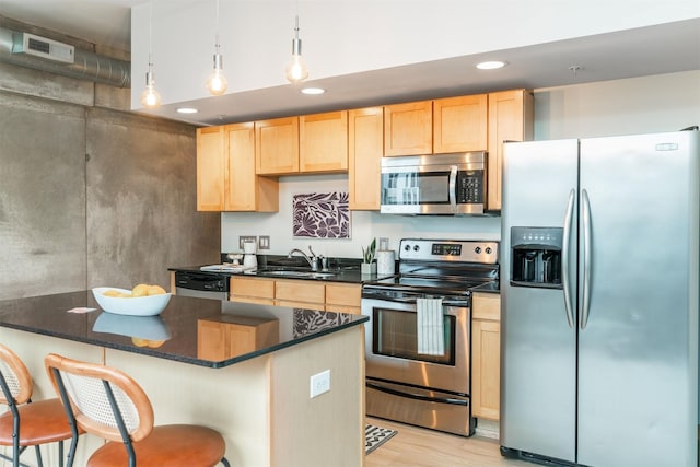 kitchen featuring sink, stainless steel appliances, a kitchen bar, decorative light fixtures, and light wood-type flooring