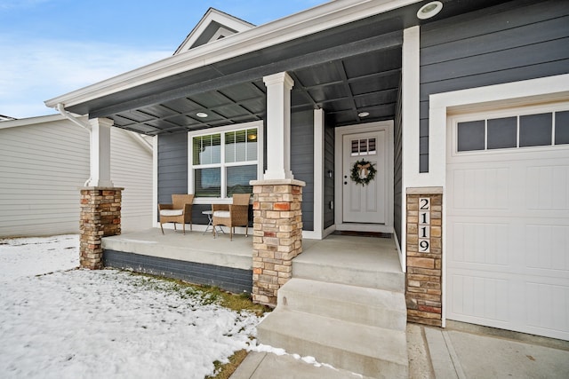 snow covered property entrance featuring covered porch and a garage