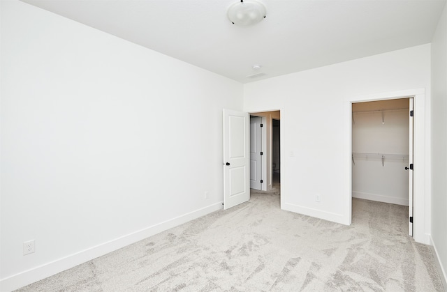 unfurnished bedroom featuring a spacious closet, light carpet, and a closet