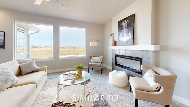 living room with a tiled fireplace, ceiling fan, light carpet, and a textured ceiling