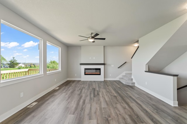 16409 Deerview Dr, Urbandale, IA 50323 - unfurnished living room featuring a glass covered fireplace, stairs, a ceiling fan, baseboards, and wood finished floors