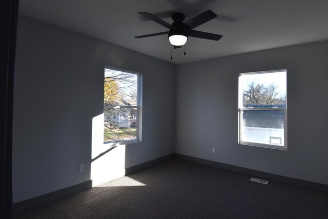 spare room with dark carpet, plenty of natural light, and ceiling fan