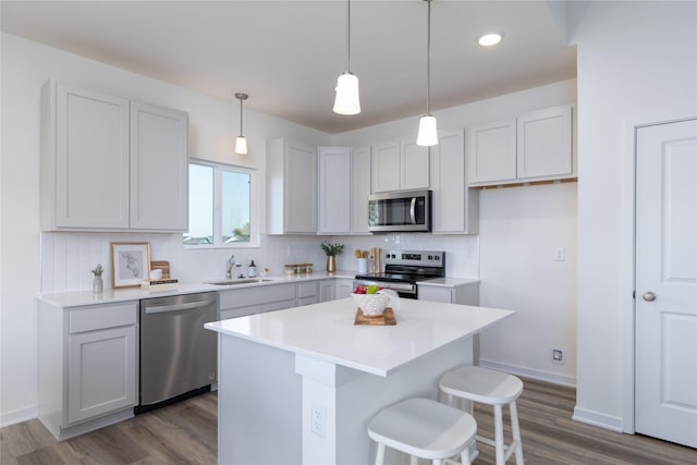 kitchen with appliances with stainless steel finishes, a center island, tasteful backsplash, pendant lighting, and dark wood-type flooring