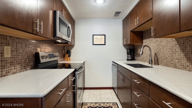 kitchen featuring decorative backsplash, sink, light tile patterned floors, and appliances with stainless steel finishes