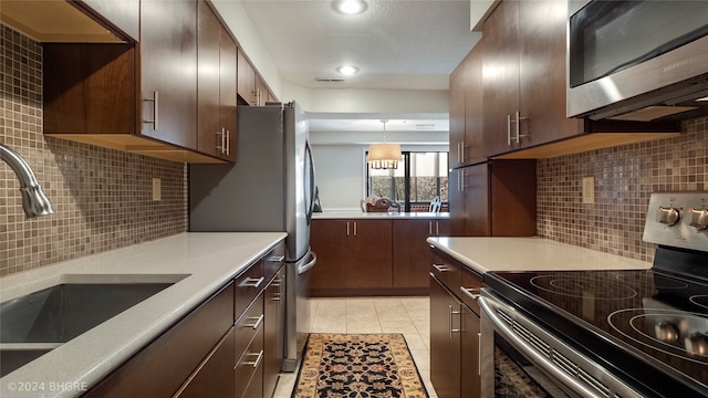 kitchen with sink, light tile patterned floors, appliances with stainless steel finishes, tasteful backsplash, and decorative light fixtures