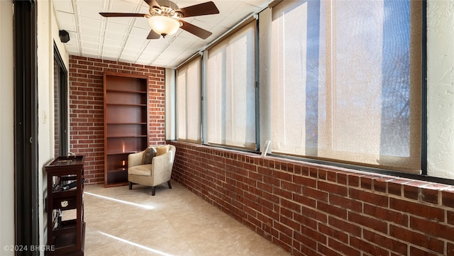 sitting room featuring ceiling fan, brick wall, and a wealth of natural light