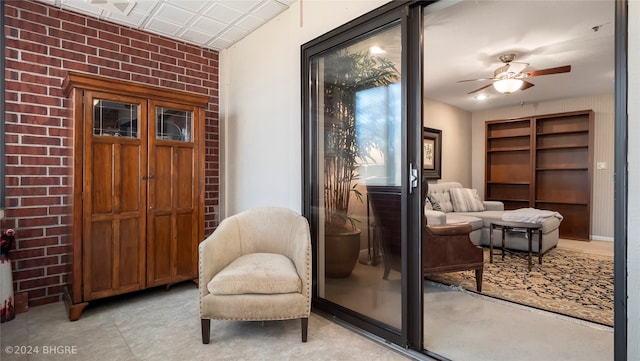 sitting room featuring ceiling fan and brick wall