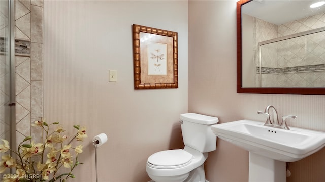 bathroom featuring toilet, a shower with shower door, and sink