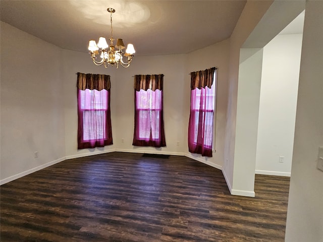 spare room featuring an inviting chandelier and dark wood-type flooring