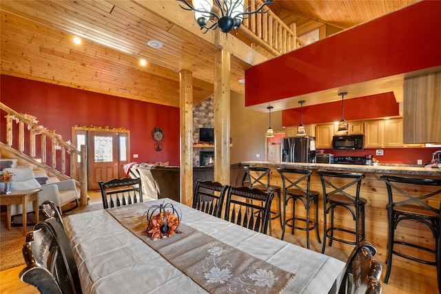 dining space featuring light wood-type flooring, wood ceiling, high vaulted ceiling, a fireplace, and a chandelier