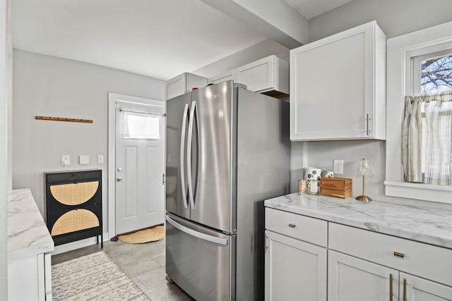 kitchen with light stone countertops, stainless steel fridge, white cabinetry, and light tile patterned flooring