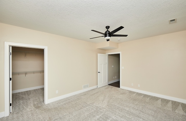 unfurnished bedroom featuring ceiling fan, a spacious closet, light colored carpet, a textured ceiling, and a closet