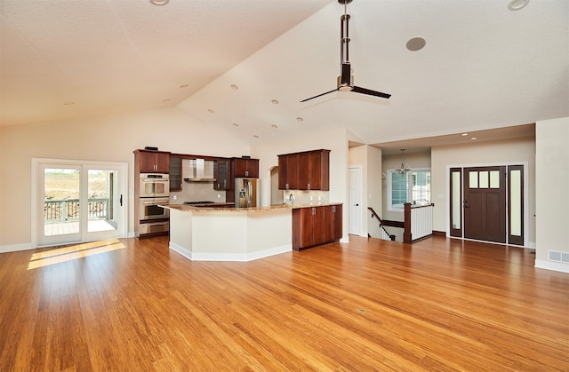 kitchen with hanging light fixtures, wall chimney range hood, lofted ceiling, appliances with stainless steel finishes, and light wood-type flooring