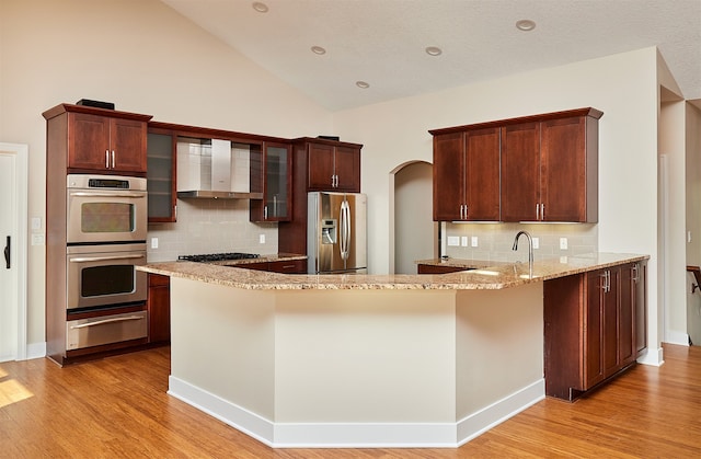 kitchen featuring decorative backsplash, appliances with stainless steel finishes, light hardwood / wood-style floors, and kitchen peninsula