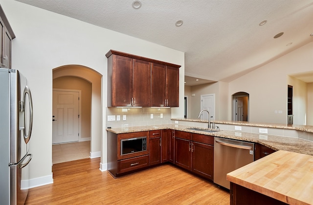 kitchen featuring kitchen peninsula, light wood-type flooring, stainless steel appliances, sink, and butcher block counters