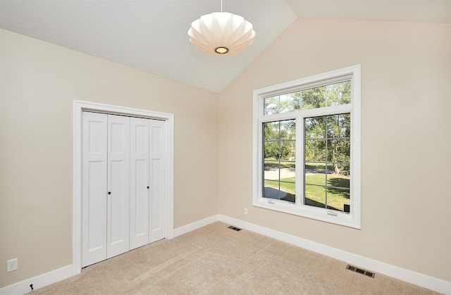 unfurnished bedroom with light colored carpet, vaulted ceiling, and a closet