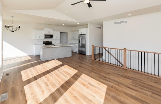 kitchen with an island with sink, wood-type flooring, vaulted ceiling, and appliances with stainless steel finishes