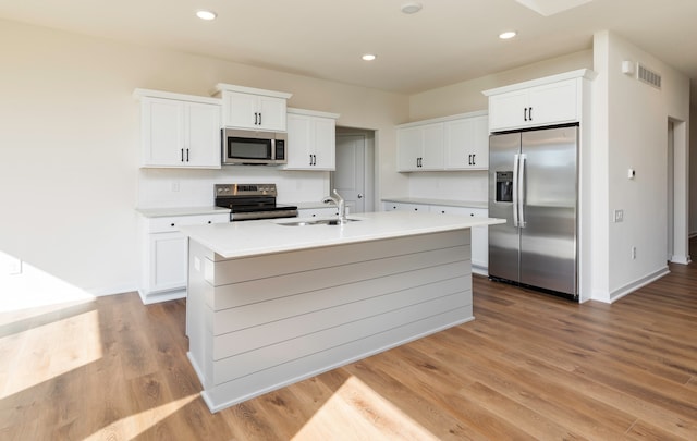 kitchen with appliances with stainless steel finishes, white cabinetry, and an island with sink