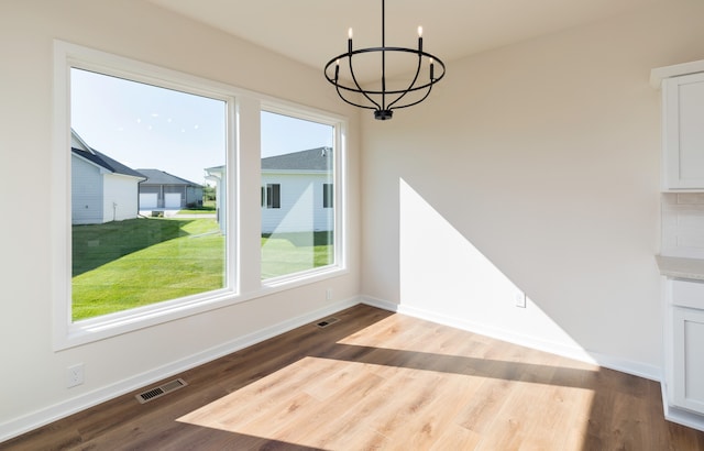 unfurnished dining area featuring a wealth of natural light, hardwood / wood-style floors, and a notable chandelier