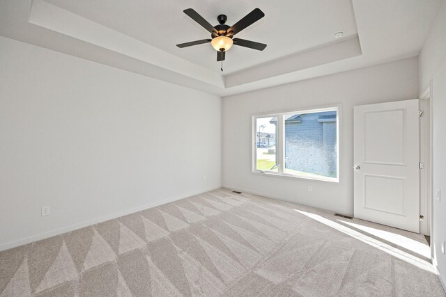 empty room featuring ceiling fan, light colored carpet, and a tray ceiling