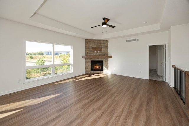 unfurnished living room featuring hardwood / wood-style flooring, ceiling fan, a stone fireplace, and a tray ceiling