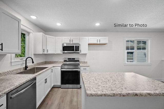 kitchen with appliances with stainless steel finishes, sink, light hardwood / wood-style flooring, white cabinets, and a kitchen island