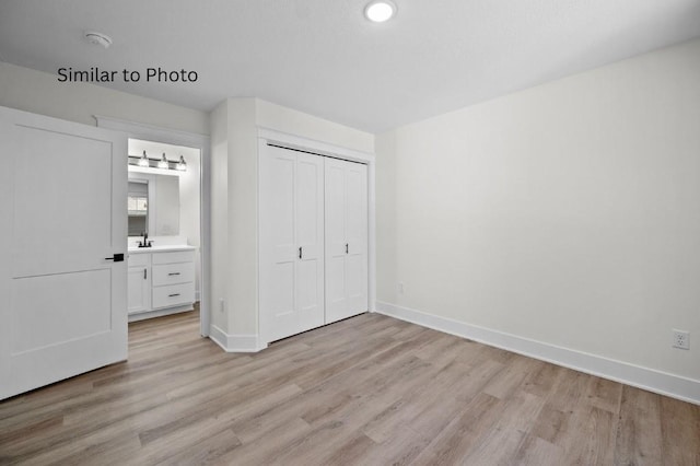 unfurnished bedroom featuring ensuite bathroom, a closet, and light hardwood / wood-style floors