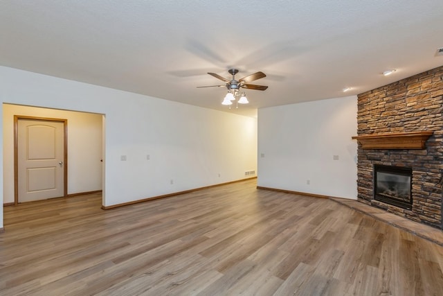 unfurnished living room with light hardwood / wood-style flooring, a stone fireplace, and ceiling fan