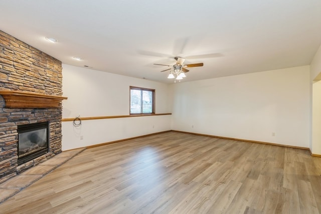 unfurnished living room with ceiling fan, a stone fireplace, and light hardwood / wood-style flooring