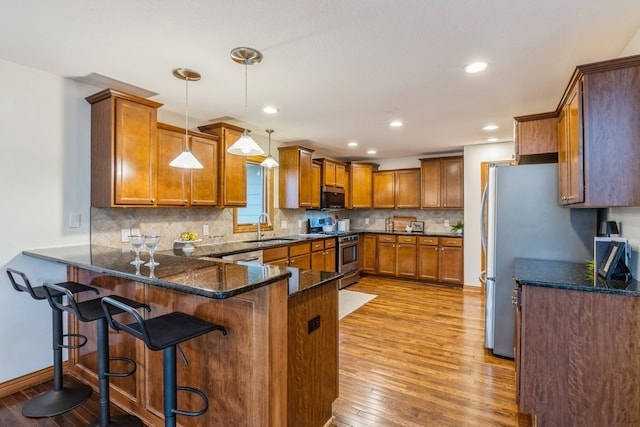 kitchen featuring kitchen peninsula, appliances with stainless steel finishes, light wood-type flooring, a kitchen bar, and pendant lighting