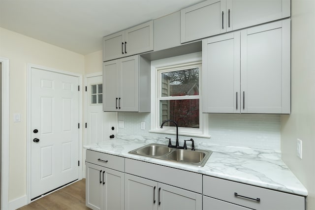 kitchen with decorative backsplash, light hardwood / wood-style floors, light stone countertops, and sink