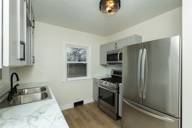 kitchen featuring light stone countertops, appliances with stainless steel finishes, sink, gray cabinets, and light hardwood / wood-style floors