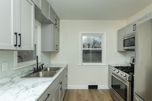 kitchen featuring sink, light stone counters, backsplash, light hardwood / wood-style floors, and appliances with stainless steel finishes