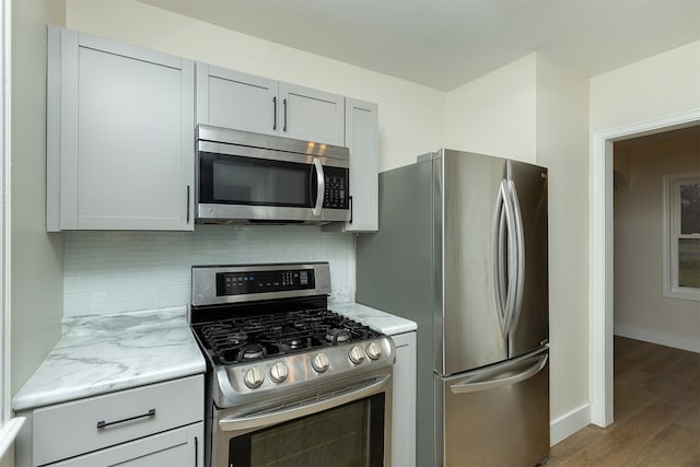 kitchen featuring decorative backsplash, light hardwood / wood-style floors, light stone counters, and stainless steel appliances