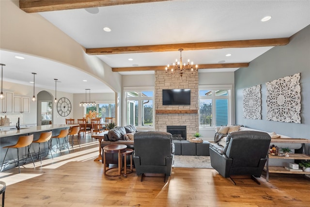 living room featuring a brick fireplace, light hardwood / wood-style flooring, beamed ceiling, and an inviting chandelier