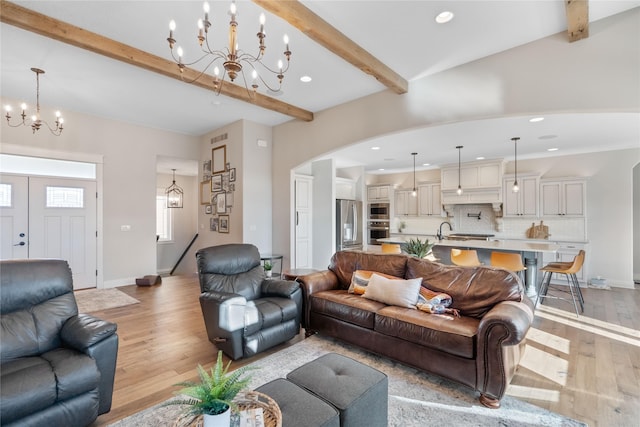 living room featuring beamed ceiling, a chandelier, and light hardwood / wood-style flooring