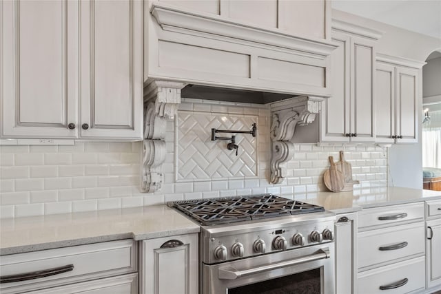 kitchen with white cabinetry, decorative backsplash, stainless steel gas stove, and light stone countertops