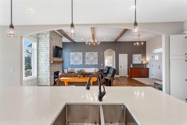 kitchen with light stone countertops, pendant lighting, beamed ceiling, sink, and a brick fireplace