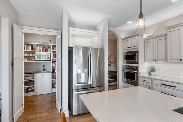 kitchen with tasteful backsplash, pendant lighting, sink, light wood-type flooring, and stainless steel appliances