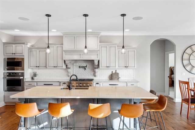 kitchen with hanging light fixtures, a kitchen island with sink, appliances with stainless steel finishes, and a kitchen breakfast bar