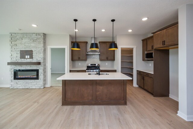 kitchen featuring stainless steel appliances, sink, decorative light fixtures, a fireplace, and a center island with sink