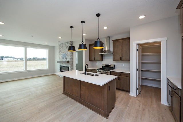 kitchen with sink, decorative light fixtures, stainless steel range with gas cooktop, a kitchen island with sink, and wall chimney range hood