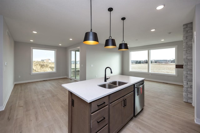 kitchen with sink, a kitchen island with sink, hanging light fixtures, stainless steel dishwasher, and light wood-type flooring