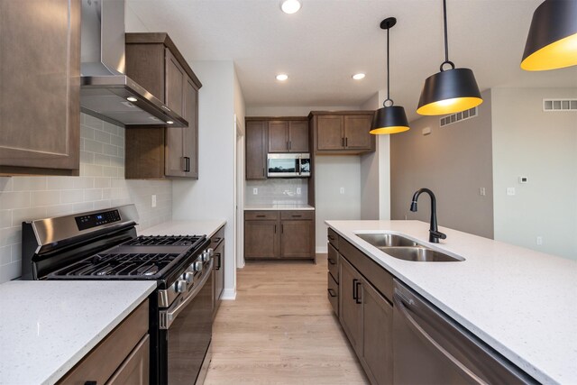 kitchen featuring light stone counters, decorative light fixtures, stainless steel appliances, wall chimney range hood, and sink