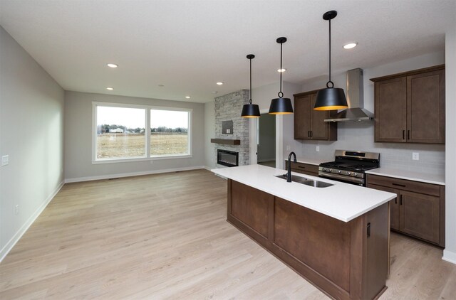 kitchen featuring a center island with sink, stainless steel gas range oven, pendant lighting, sink, and wall chimney range hood