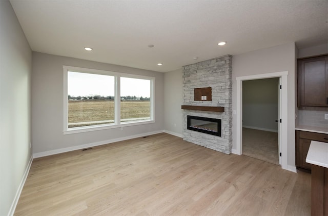 unfurnished living room featuring a stone fireplace and light wood-type flooring